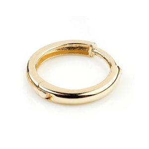 Könnte beinhalten: Ein polierter goldener Creolen-Ohrring mit einer glatten, abgerundeten Oberfläche und einem Klappverschluss. Das kreisförmige Schmuckstück verfügt über eine reflektierende metallische Oberfläche und ein schlichtes, durchgehendes Design.