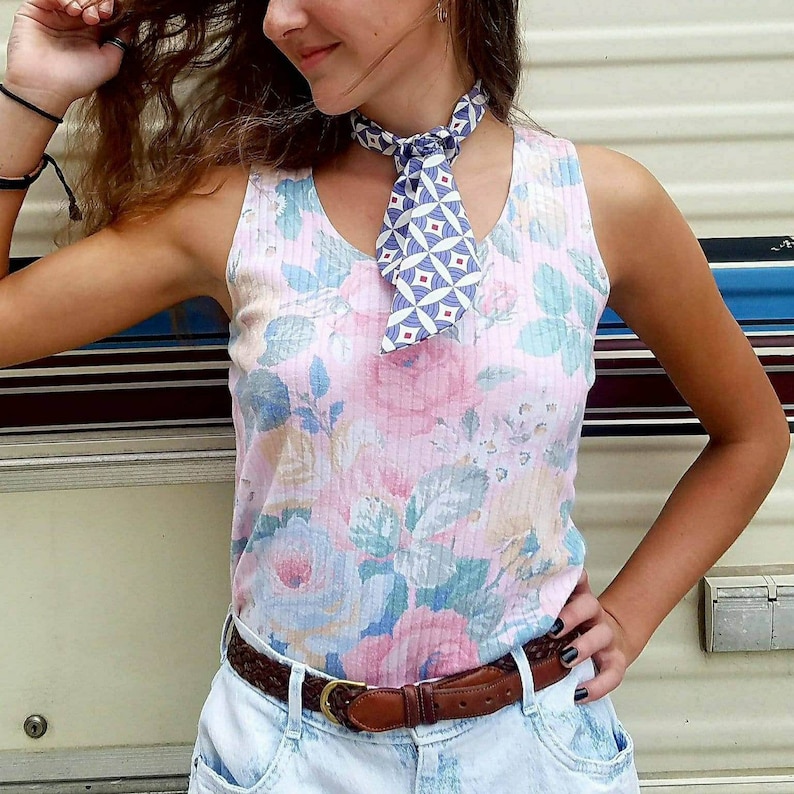 May include: A woman wearing a pink and white floral tank top with a blue and white patterned neck scarf and a brown belt.