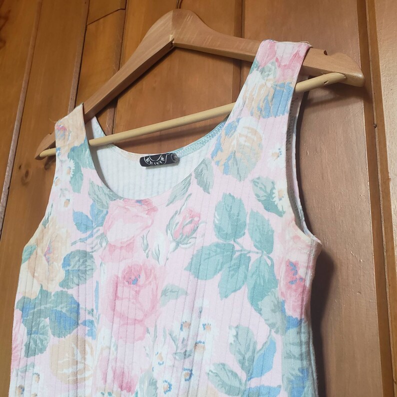 May include: A sleeveless, pink and white floral print top with a ribbed texture. The top has a scoop neck and a small black tag with the word "River" on it.