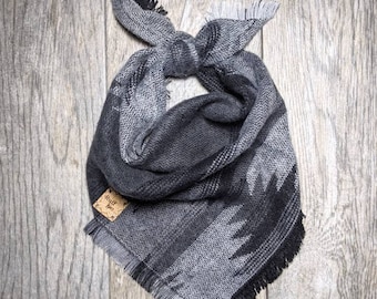 May include: A gray and black bandana with a fringed edge. The bandana is tied in a knot and has a small brown tag that says "Wolf Tree".
