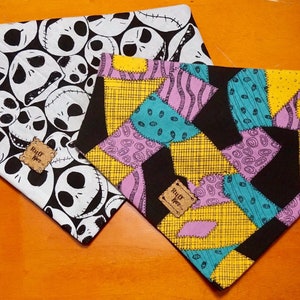 May include: Two dog bandanas with a patchwork design. One bandana features a black and white pattern of Jack Skellington's face from the Nightmare Before Christmas. The other bandana features a colorful patchwork design with yellow, pink, blue, and green. Both bandanas have a brown tag that says "Ruff Wear".