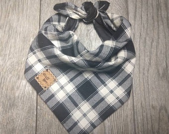 May include: A black and white plaid dog bandana with a knotted closure. The bandana features a woven pattern and a small, rectangular tag with the text "Ruff Ware". The fabric is a mix of black and white squares.