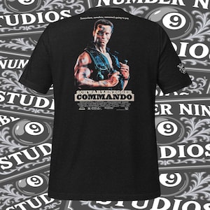 Puede incluir: Camiseta negra con una imagen de Arnold Schwarzenegger de la película "Commando". El diseño incluye el título de la película y una cita. La camiseta tiene mangas cortas y cuello redondo.