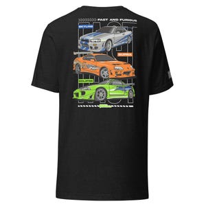 Peut inclure: T-shirt gris foncé avec un motif de trois voitures : une Skyline argentée, une Supra orange et une Eclipse verte. Le texte "FAST AND FURIOUS" est au-dessus des voitures. Le t-shirt a un col rond et des manches courtes.
