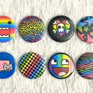 May include: A collection of eight colorful round buttons with various designs. The designs include a rainbow-colored face, leopard print, a skull with a rainbow heart, stars, a Nyan Cat, a checkered pattern, a meme face, and a zebra pattern.
