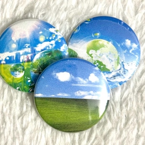 May include: Three round buttons with landscape designs. One button features a blue sky with white clouds over a green field. The other two buttons have similar designs with blue skies, green fields, and water droplets.