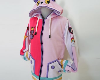 May include: A zip-up hoodie featuring a split design of hot pink and light pink. The hood includes animal ears with purple accents and a face graphic. The sleeves and front display colourful patches including a crown, star, heart, and rainbow.