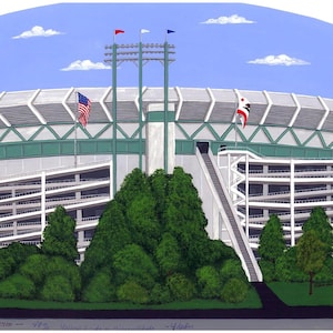 May include: An illustration of Candlestick Park in San Francisco, California. The stadium is depicted with a green and white color scheme, with American and other flags waving. The sky is blue with white clouds, and green trees are in the foreground.