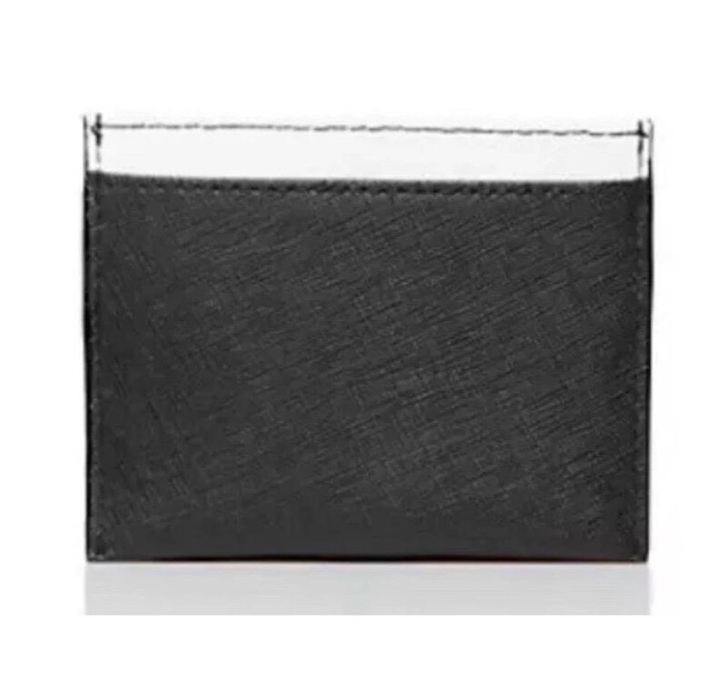 May include: A black card holder with a textured surface and a white top section. The card holder is rectangular and appears to be made of leather or a similar material. The stitching is visible along the top edge.