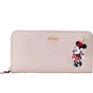 May include: A light pink wallet with a zipper closure and a Minnie Mouse design. The wallet features a cartoon Minnie Mouse wearing a red polka dot dress and a matching bow. The Kate Spade logo is visible.
