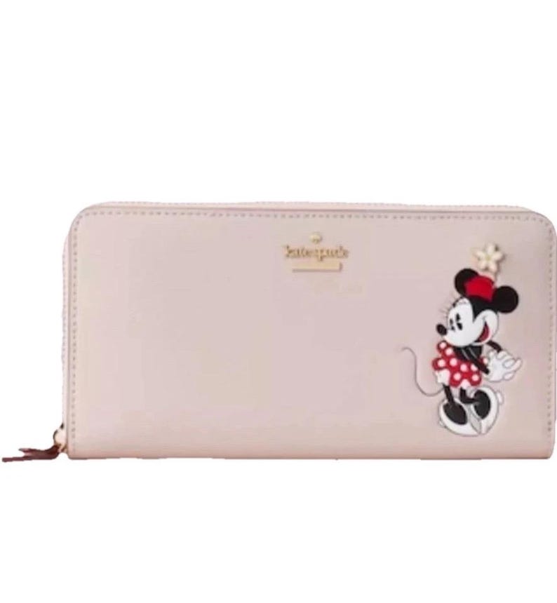 May include: A light pink wallet with a zipper closure and a Minnie Mouse design. The wallet features a cartoon Minnie Mouse wearing a red polka dot dress and a matching bow. The Kate Spade logo is visible.