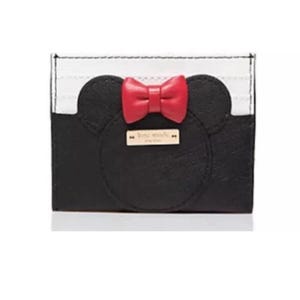 May include: Black and white cardholder with a Minnie Mouse design. The cardholder features a black face with two rounded ears and a red bow. A small gold rectangular tag is centered below the bow.