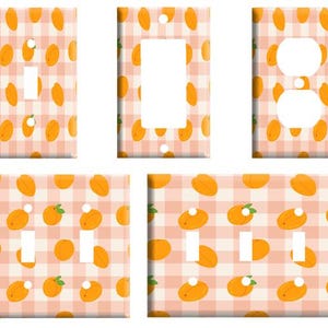 May include: A collection of five light switch and outlet wall plates featuring a repeating pattern of orange fruit on a light pink and white checkered background. The set includes various configurations for single switches, rockers, and duplex outlets.