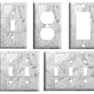 May include: Set of five white marble-patterned light switch and outlet covers. The covers feature a realistic marble design with gray veining. The set includes one single switch cover, one double switch cover, one outlet cover, and two triple switch covers.