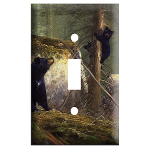 May include: A light switch cover featuring a painting of two black bears in a forest setting. The larger bear is standing on the ground, while the smaller bear is climbing a tree. The background is a lush green forest with a rocky outcropping.