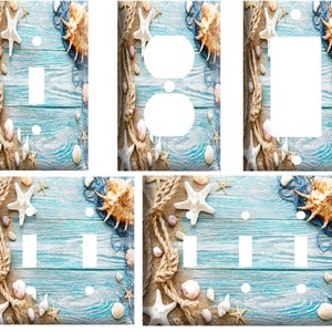 May include: Coastal-themed light switch covers and outlet covers. The designs feature a light blue wood grain background, adorned with seashells, starfish, and rope accents. The covers are available in various configurations, including single switch, double switch, and outlet styles.