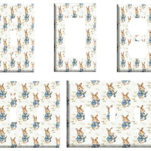 May include: Set of four light switch covers featuring a repeating pattern of Peter Rabbit illustrations. The covers are white with a light blue background and feature Peter Rabbit in a blue jacket holding a carrot.