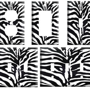 May include: A set of five electrical wall plates with a black and white zebra stripe pattern. The plates include configurations for outlets, light switches, and a single rocker switch. The design is a bold, animal print style.
