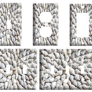 May include: A collection of five rectangular wall plates for electrical switches and outlets, each featuring a repeating pattern of small, light gray and white spiral seashells densely packed across the entire surface of the plates.
