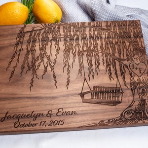 May include: A wooden cutting board with an engraved design of a weeping willow tree with a swing hanging from its branches. The board is personalized with the names "Jacquelyn & Evan" and the date "October 17, 2015".