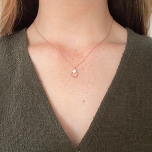 May include: A delicate rose gold necklace with a small, white pearl pendant. The pendant is set in a simple, geometric design.