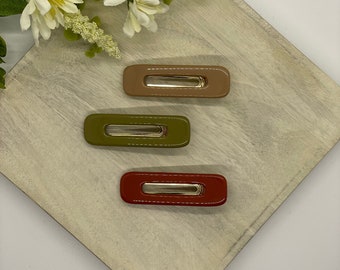 May include: Three rectangular hair clips in different colors: brown, green, and red. The clips are made of plastic and have a shiny finish.