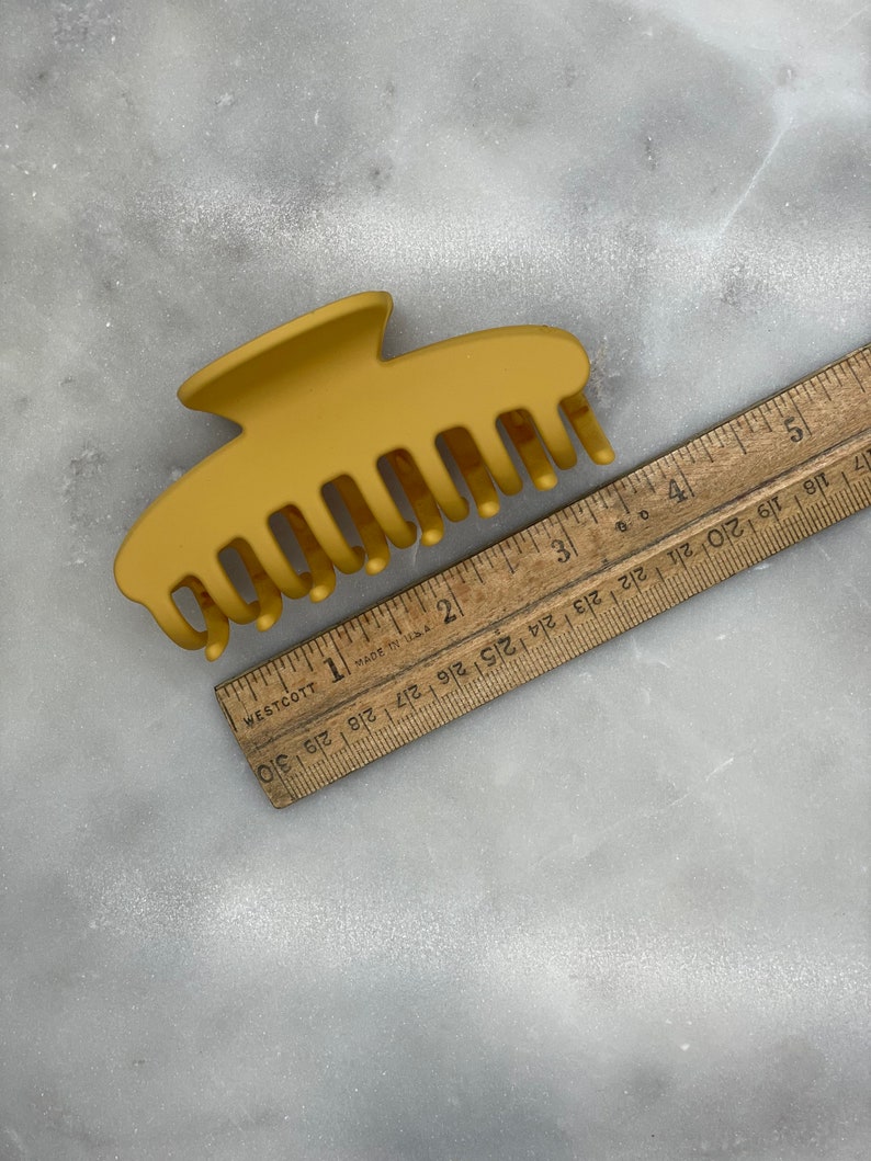Peut inclure: Une pince &agrave; cheveux en plastique jaune moutarde avec une finition lisse. La pince mesure environ 7,5 cm de long et poss&egrave;de 7 dents.