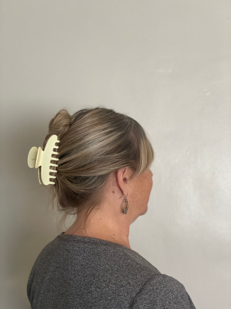Peut inclure: Une personne aux cheveux bruns portant une chemise grise et une grande pince &agrave; cheveux en plastique blanc cass&eacute;.