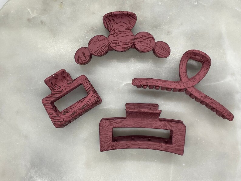 May include: Four burgundy hair clips with a wood grain texture. The clips are in different shapes and sizes.