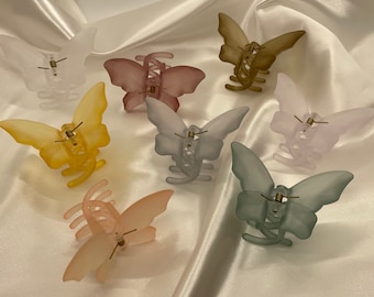 May include: Assortment of eight butterfly hair clips in various pastel colors, including light pink, yellow, light blue, gray, and brown. The clips are made of plastic and have a spring-loaded mechanism.