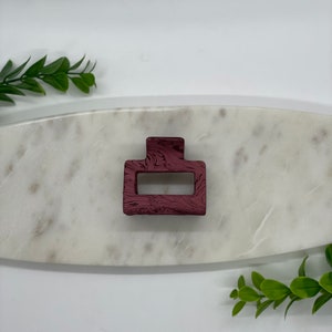 May include: A burgundy hair clip with a swirl pattern. The clip is rectangular with a rounded top and bottom.