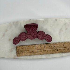 May include: A burgundy plastic hair claw with a wavy pattern. The claw has five rounded sections.