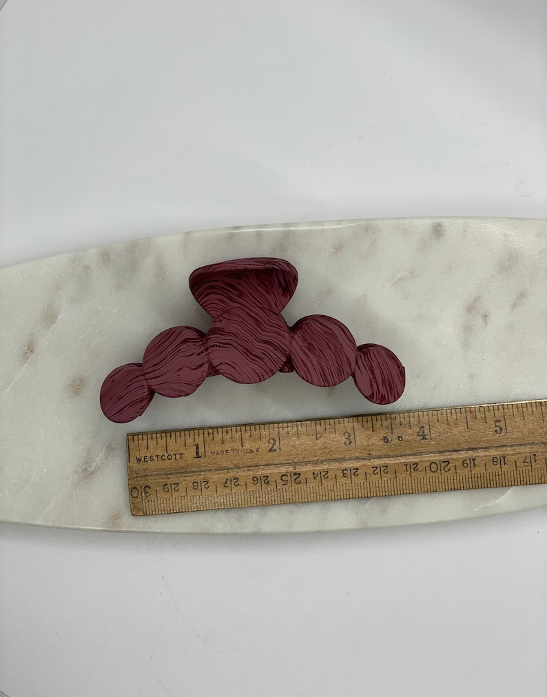 May include: A burgundy plastic hair claw with a wavy pattern. The claw has five rounded sections.