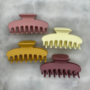 Peut inclure: Quatre pinces &agrave; cheveux en plastique de diff&eacute;rentes couleurs&nbsp;: mauve, jaune moutarde, cr&egrave;me et bordeaux. Chaque pince a une forme lisse et arrondie avec une s&eacute;rie de dents le long du bord inf&eacute;rieur.