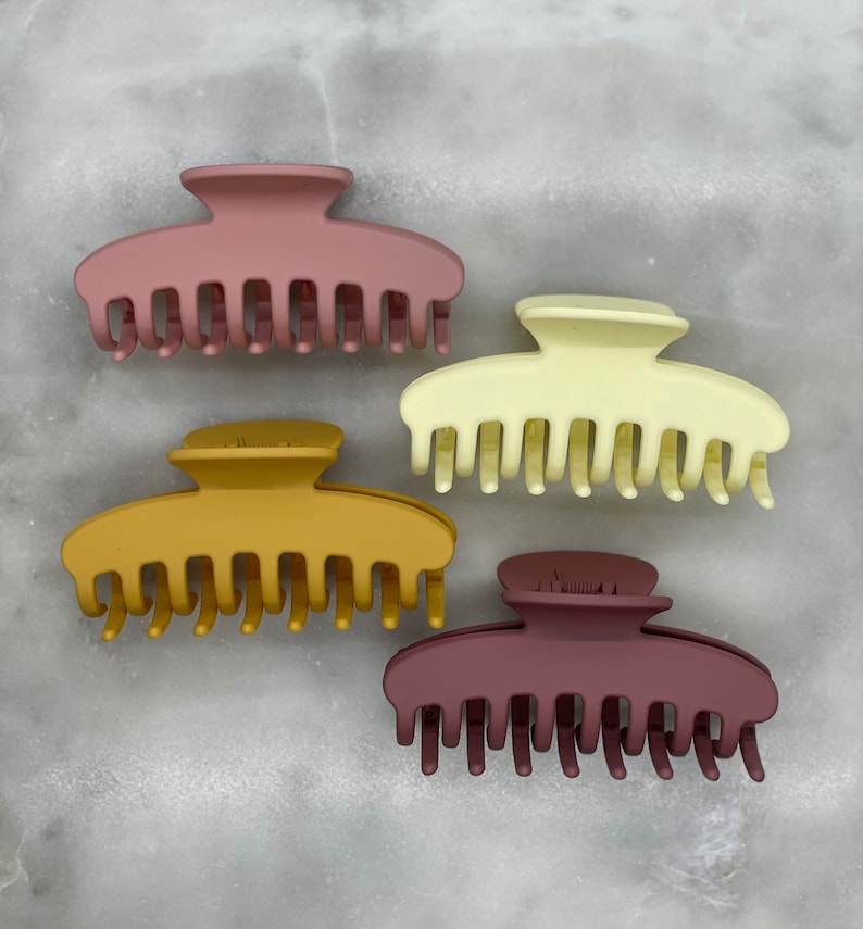 Peut inclure: Quatre pinces &agrave; cheveux en plastique de diff&eacute;rentes couleurs&nbsp;: mauve, jaune moutarde, cr&egrave;me et bordeaux. Chaque pince a une forme lisse et arrondie avec une s&eacute;rie de dents le long du bord inf&eacute;rieur.
