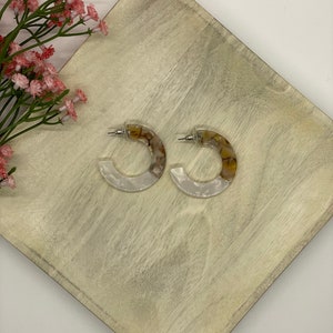 May include: A pair of white and brown hoop earrings with a marbled pattern.