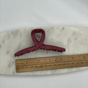 May include: A burgundy plastic hair claw with a textured surface. The claw is approximately 3 inches long.