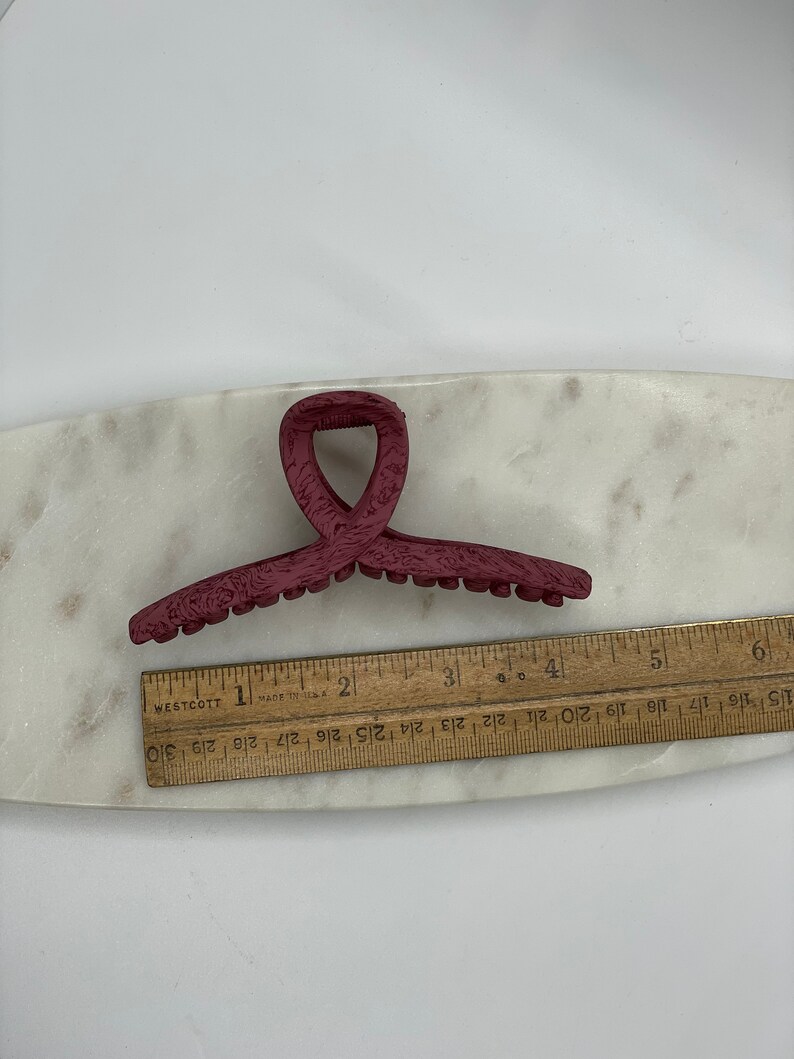 May include: A burgundy plastic hair claw with a textured surface. The claw is approximately 3 inches long.