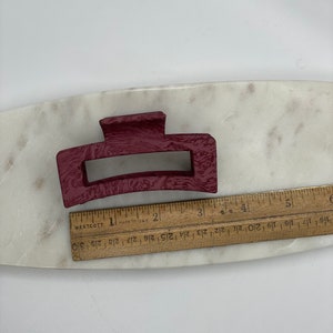May include: A burgundy plastic hair claw clip. The clip is approximately 3 inches long.