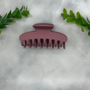 Peut inclure: Une grande pince &agrave; cheveux en plastique brun fonc&eacute; avec une finition mate lisse. La pince a une base large et plate et une s&eacute;rie de dents qui s'embo&icirc;tent pour maintenir les cheveux en place.
