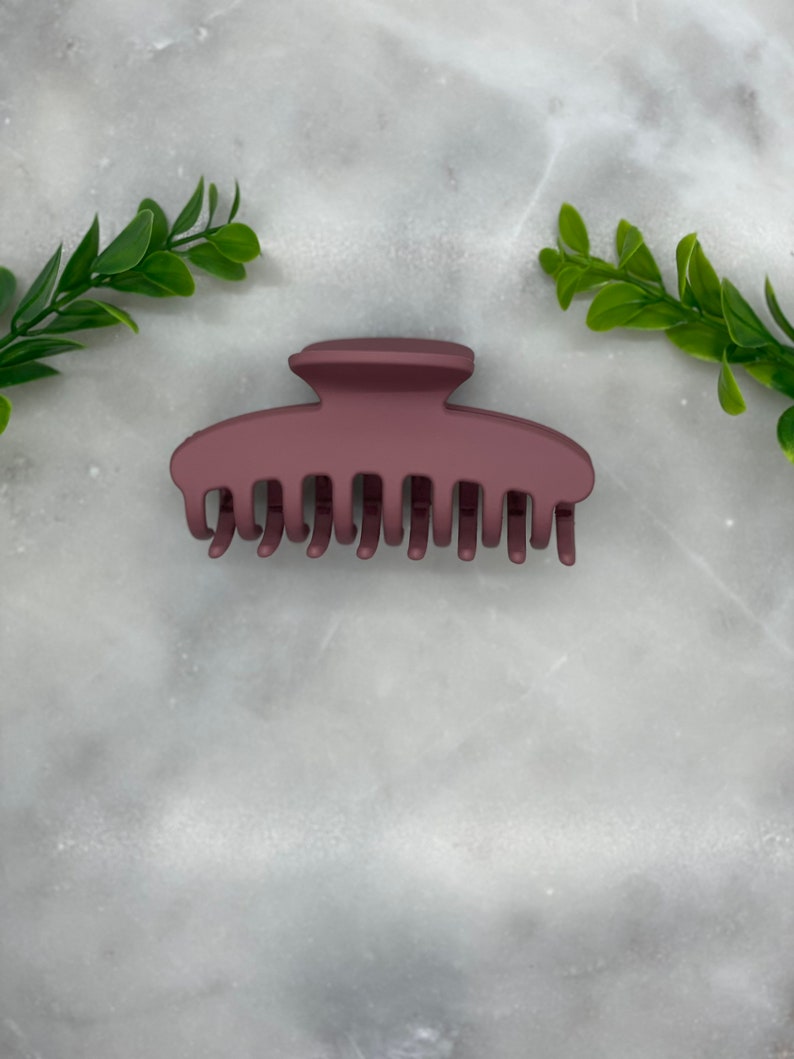 Peut inclure: Une grande pince &agrave; cheveux en plastique brun fonc&eacute; avec une finition mate lisse. La pince a une base large et plate et une s&eacute;rie de dents qui s'embo&icirc;tent pour maintenir les cheveux en place.