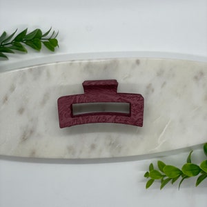 May include: A burgundy plastic hair claw clip. The clip is on a white marble surface.