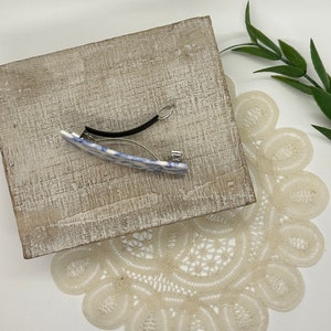 May include: A blue and white patterned hair clip with a black elastic band. The clip is on a wooden surface.