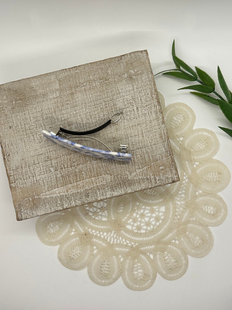 May include: A blue and white patterned hair clip with a black elastic band. The clip is on a wooden surface.