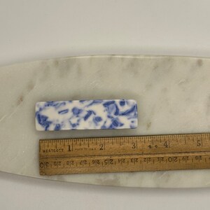May include: A blue and white ceramic hair clip with a marbled design. The clip is approximately 2 inches long.