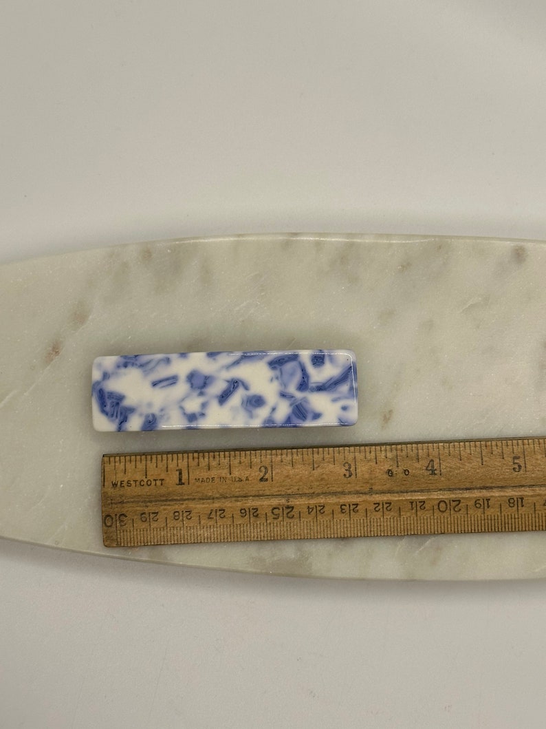 May include: A blue and white ceramic hair clip with a marbled design. The clip is approximately 2 inches long.