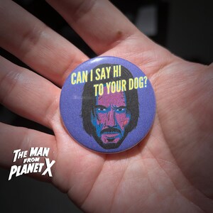 May include: A circular, purple badge with the text "CAN I SAY HI TO YOUR DOG?" and a stylized portrait of a man with black hair and a beard. The badge also features the text "The Man From Planet X" in white.