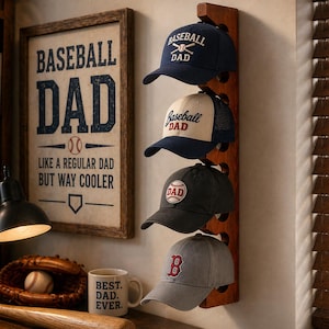 Peut inclure: Un support mural vertical en bois portant quatre casquettes de baseball. La casquette supérieure est bleu marine avec le texte blanc BASEBALL DAD. La deuxième est crème et bleu marine avec le texte Baseball DAD. La troisième est gris anthracite avec un écusson DAD circulaire. La quatrième est grise avec un B rouge.