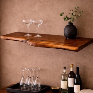 May include: A wooden shelf with a live edge, holding two coupe glasses and a black vase with greenery. Below, a cabinet displays wine bottles, a tray of glasses, and a small bowl.
