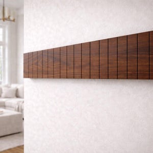 May include: A dark brown wooden wall-mounted coat rack with a series of vertical slots. The rack is rectangular and mounted on a white wall. The design is modern and minimalist, suitable for a hallway or entryway.